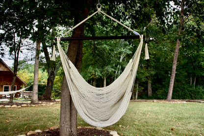 Cream Island Haven hammock chair hanging from a shade tree in a mown backyard with woods behind