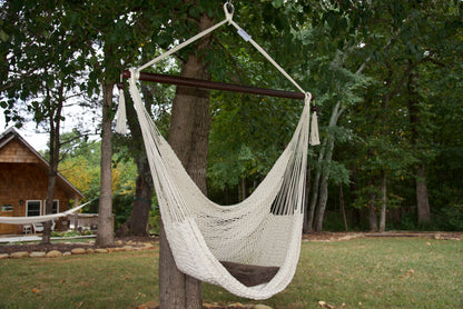 Cream Island Haven hammock chair with a brown seat pillow, hanging from a tree in a wooded backyard with a timber cabin behind
