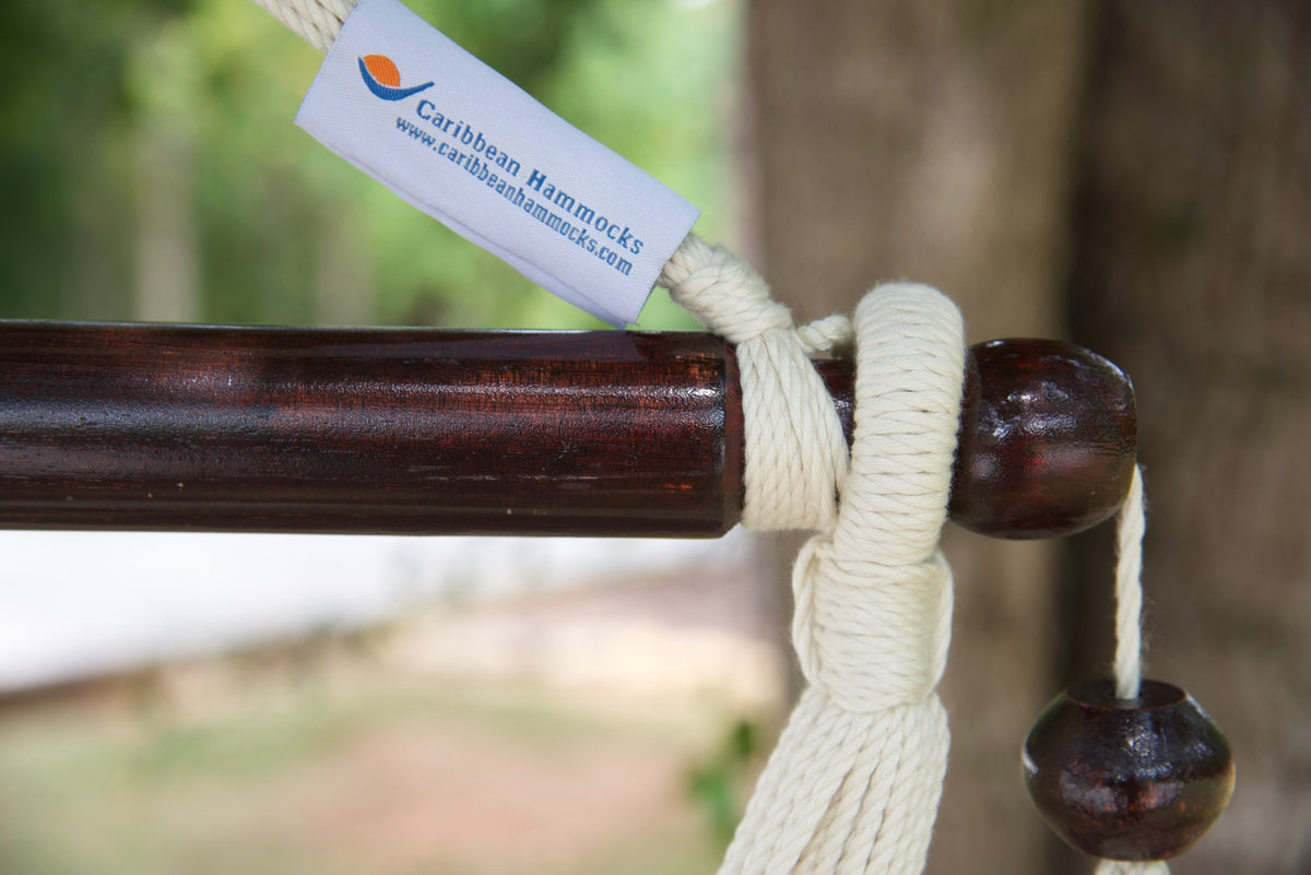 The dark varnished hardwood spreader bar of a cream Island Haven hammock chair, with end cords looped over it and a wooden bead hanging below