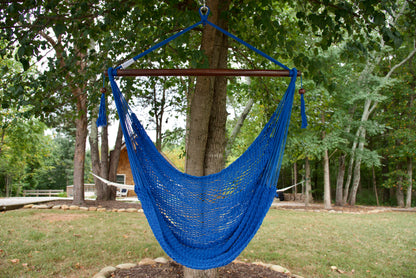 Dark blue Island Haven hammock chair hanging from a shade tree in a mown backyard with woods behind