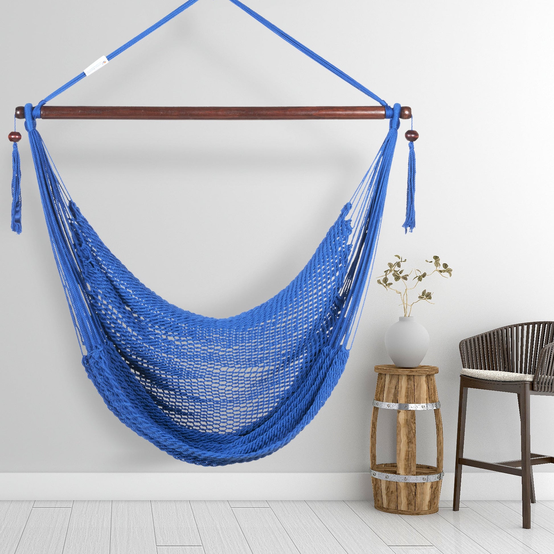 Dark blue Island Haven hammock chair hanging beside a barrel side table and bar stool against a pale grey wall