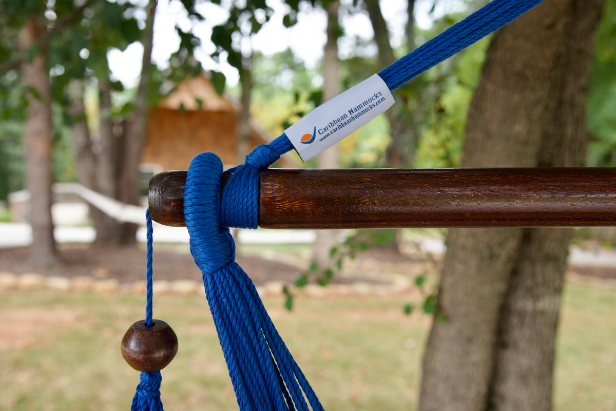 The dark varnished hardwood spreader bar of a dark blue Island Haven hammock chair, with end cords looped over it and a wooden bead hanging below