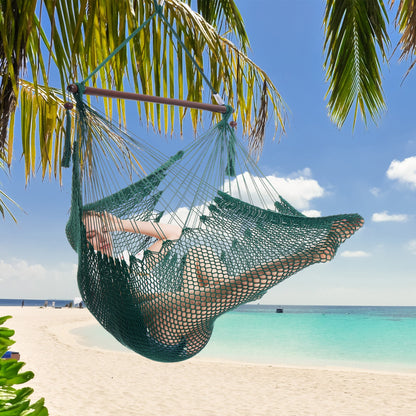 Woman resting in a green Island Haven hammock chair hung from a palm tree above a white sand beach