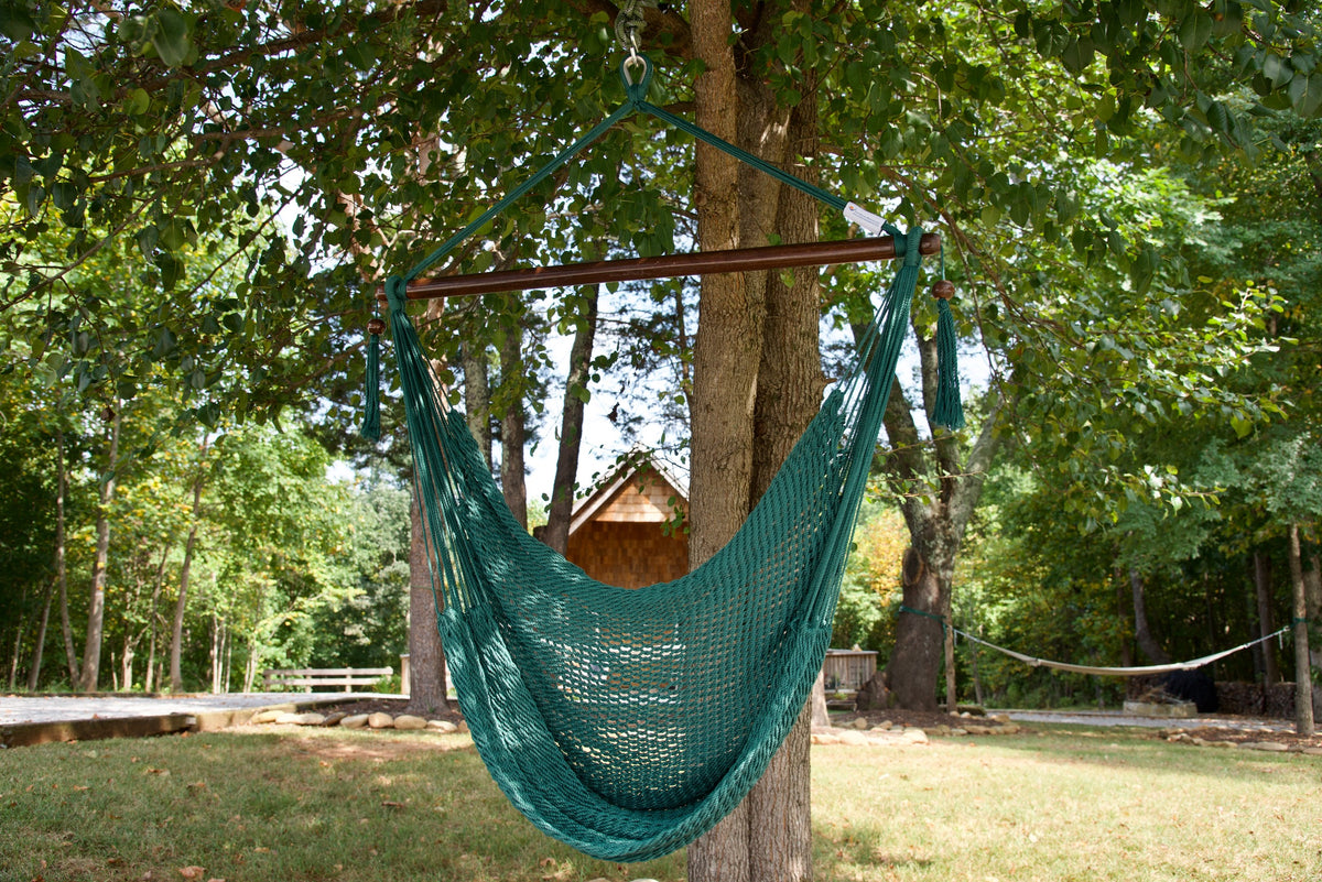 Green Island Haven hammock chair hanging from a shade tree in a mown backyard with woods behind