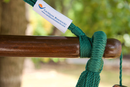 The dark varnished hardwood spreader bar of a green Island Haven hammock chair, with end cords looped over it and a wooden bead hanging below