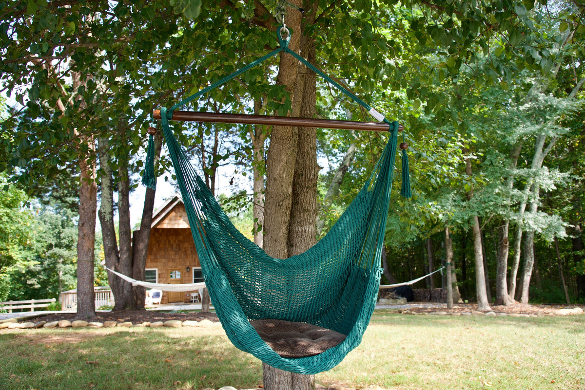 Green Island Haven hammock chair with a brown seat pillow, hanging from a tree in a wooded backyard with a timber cabin behind