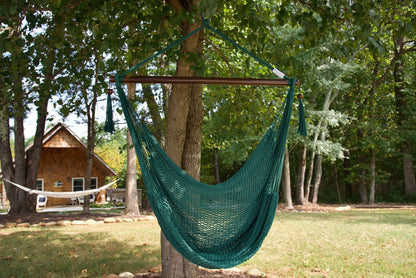 Green Island Haven hammock chair hanging from a tree in a wooded backyard, with a timber cabin and a second hammock behind