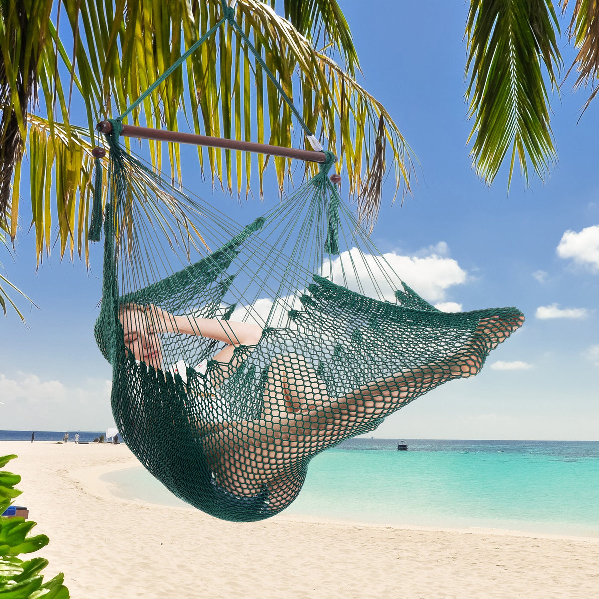 Woman resting in a green Island Haven hammock chair hung from a palm tree above a white sand beach