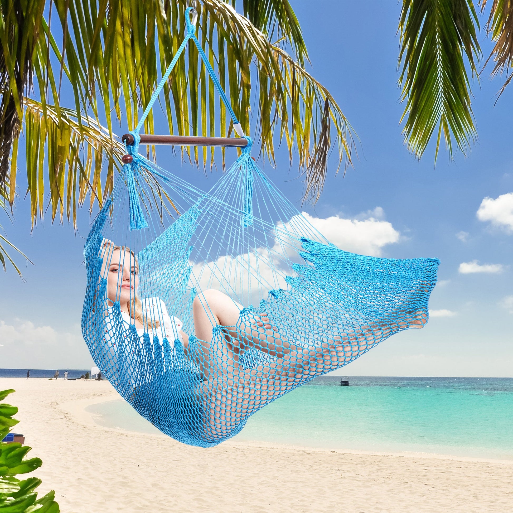 Woman resting in a light blue Island Haven hammock chair hung from a palm tree above a white sand beach