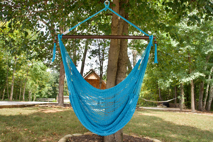 Light blue Island Haven hammock chair hanging from a shade tree in a mown backyard with woods behind