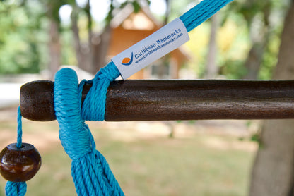 The dark varnished hardwood spreader bar of a light blue Island Haven hammock chair, with end cords looped over it and a wooden bead hanging below