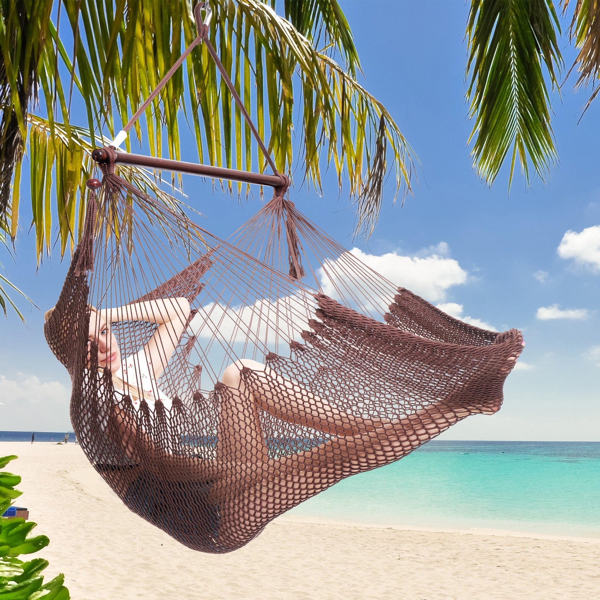 Woman resting in a mocha Island Haven hammock chair hung from a palm tree above a white sand beach