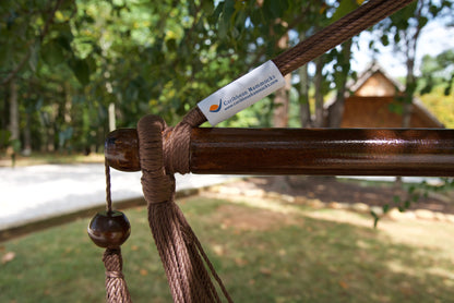 The dark varnished hardwood spreader bar of a mocha Island Haven hammock chair, with end cords looped over it and a wooden bead hanging below