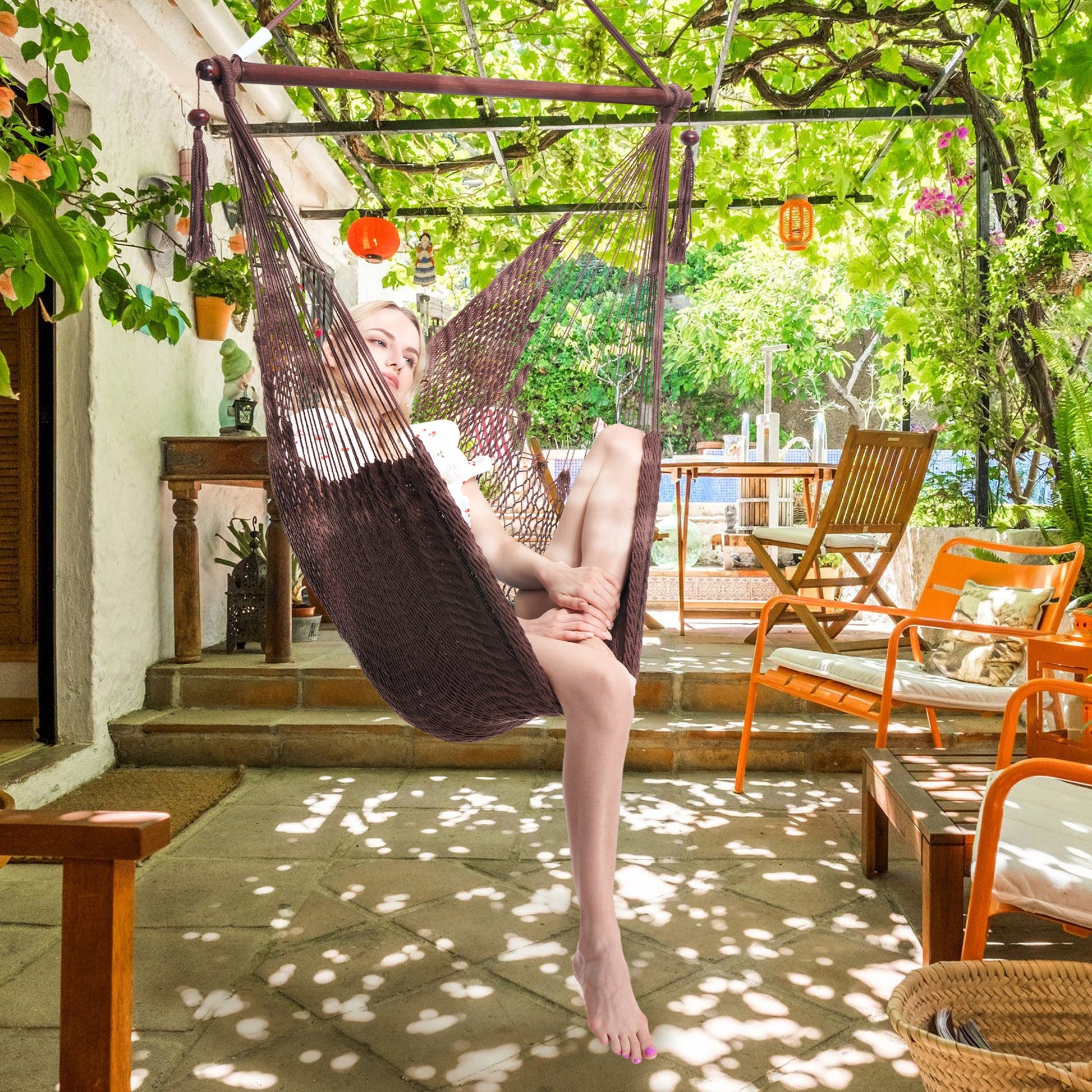 Woman seated in a mocha Island Haven hammock chair on a shaded patio under a vine-covered pergola
