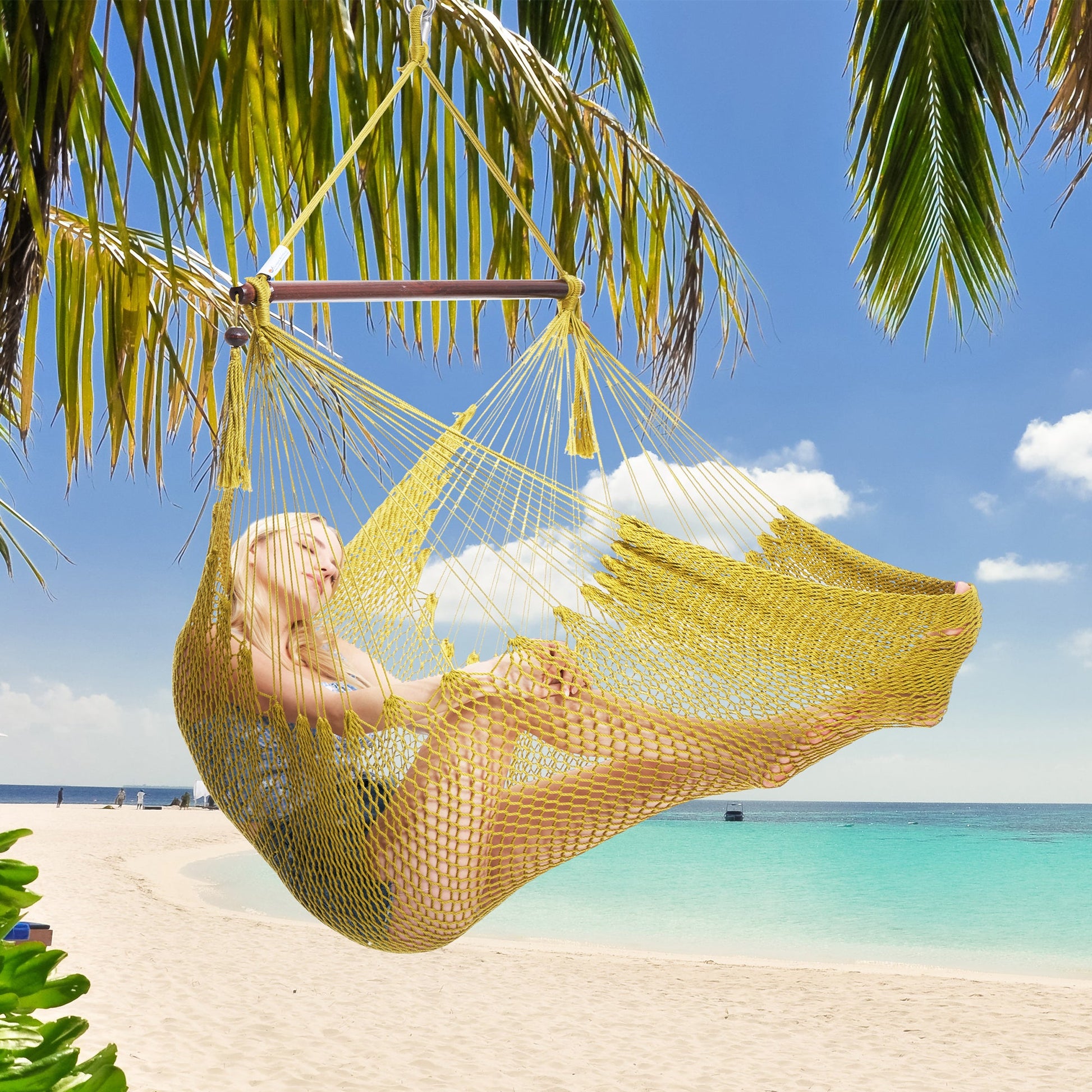 Woman resting in an olive Island Haven hammock chair hung from a palm tree above a white sand beach