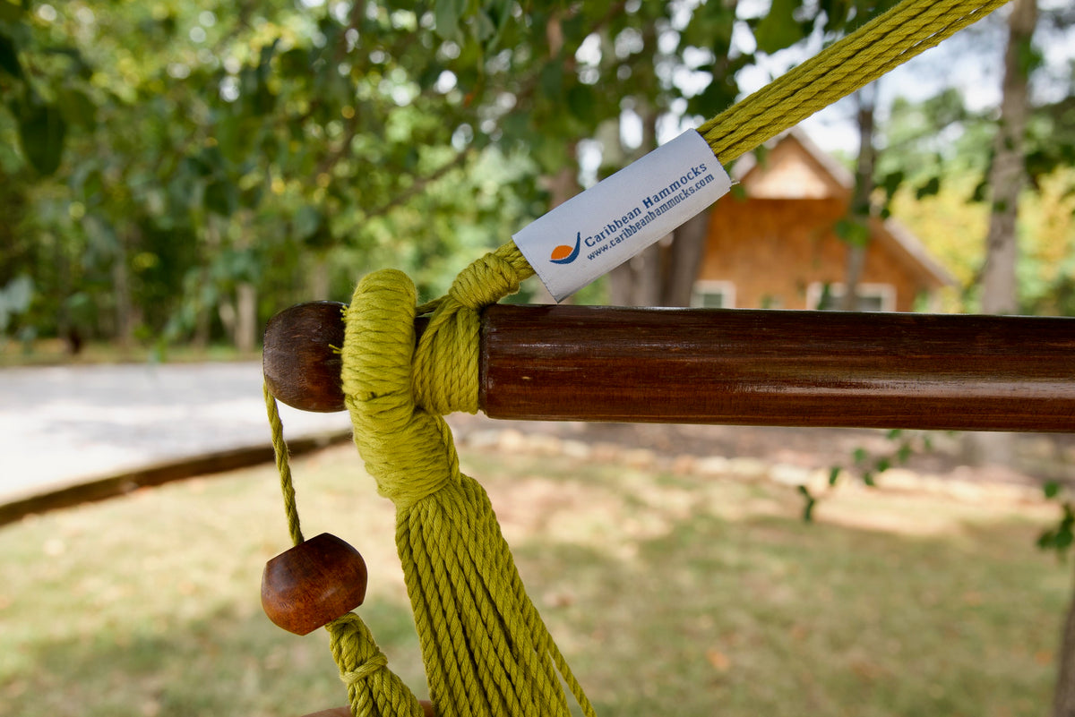 The dark varnished hardwood spreader bar of an olive Island Haven hammock chair, with end cords looped over it and a wooden bead hanging below