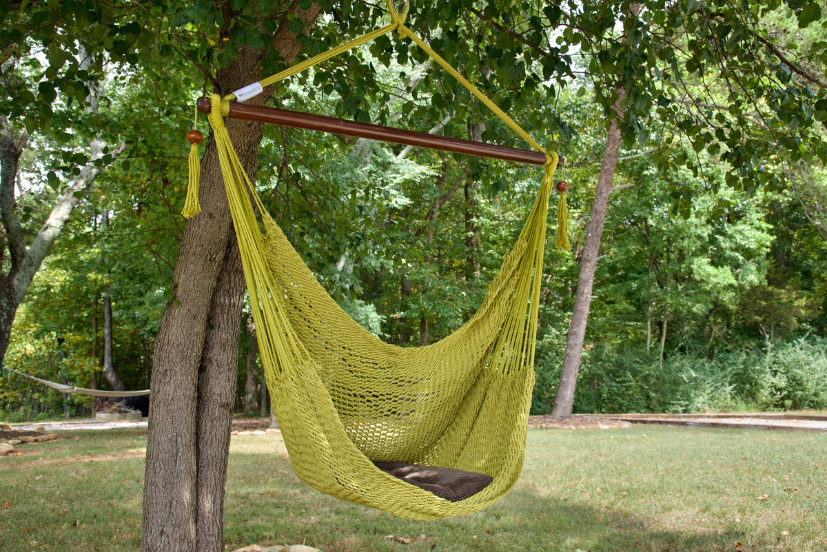 Olive Island Haven hammock chair with a brown seat pillow, hanging from a tree in a wooded backyard with a timber cabin behind