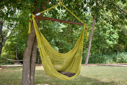 Olive Island Haven hammock chair with a brown seat pillow, hanging from a tree in a wooded backyard with a timber cabin behind