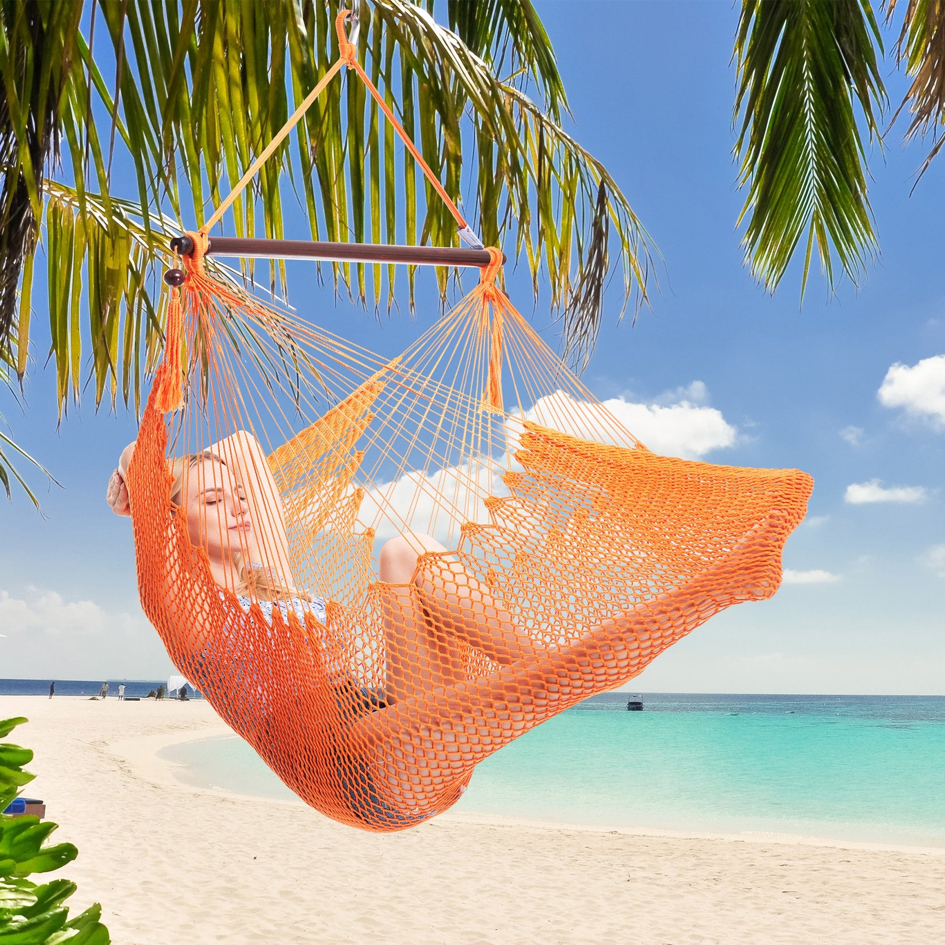 Woman resting in an orange Island Haven hammock chair hung from a palm tree above a white sand beach