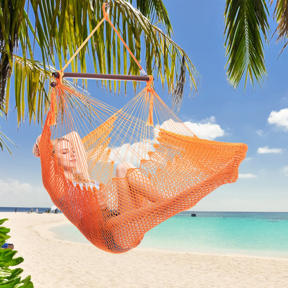 Woman resting in an orange Island Haven hammock chair hung from a palm tree above a white sand beach