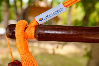 The dark varnished hardwood spreader bar of an orange Island Haven hammock chair, with end cords looped over it and a wooden bead hanging below