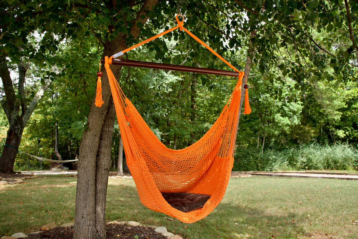 Orange Island Haven hammock chair with a brown seat pillow, hanging from a tree in a wooded backyard with a timber cabin behind
