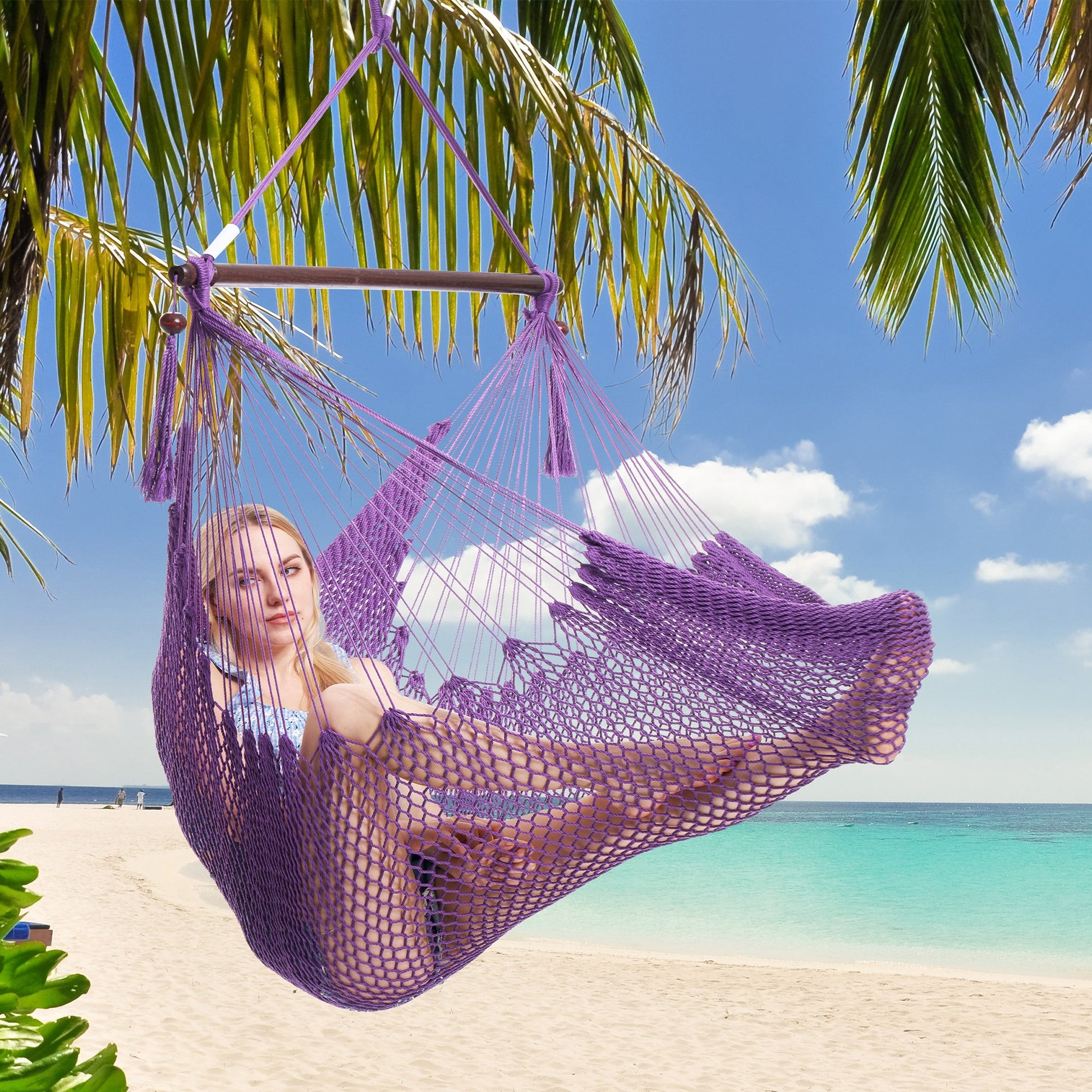 Woman resting in a purple Island Haven hammock chair hung from a palm tree above a white sand beach
