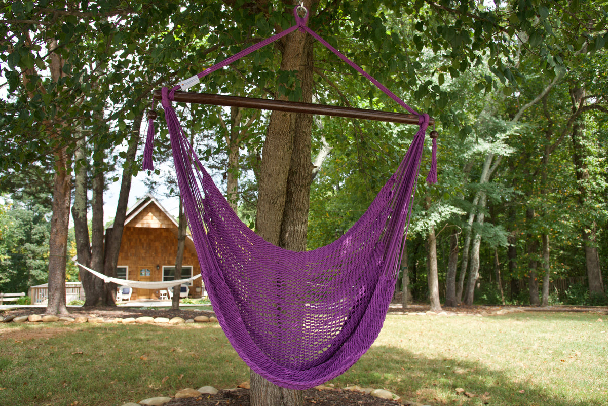 Purple Island Haven hammock chair hanging from a shade tree in a mown backyard with woods behind