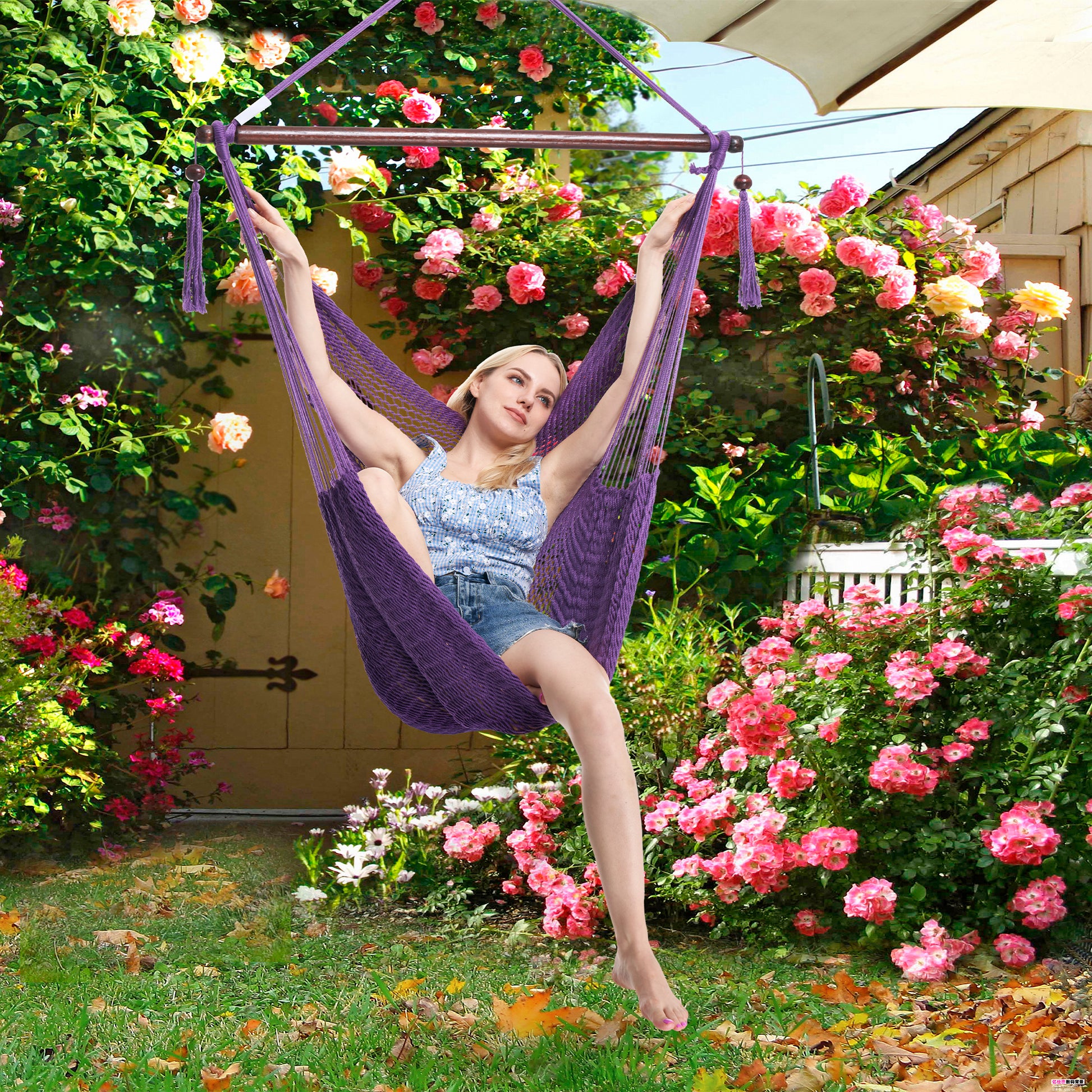 Woman reclining in a purple Island Haven hammock chair in a garden surrounded by climbing roses