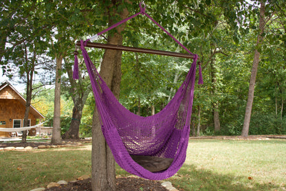 Purple Island Haven hammock chair with a brown seat pillow, hanging from a tree in a wooded backyard with a timber cabin behind