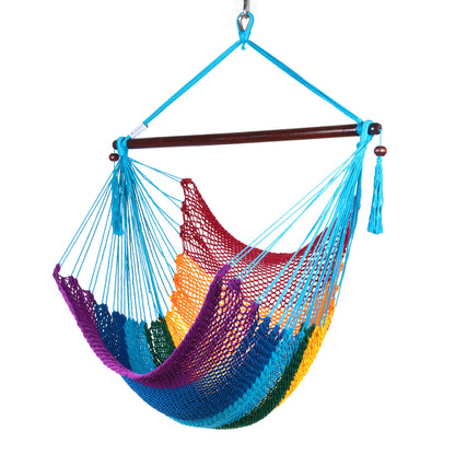 Island Haven hammock chair in rainbow, hand-woven rainbow-striped poly cord with a dark hardwood spreader bar and tasseled ends, on a white background