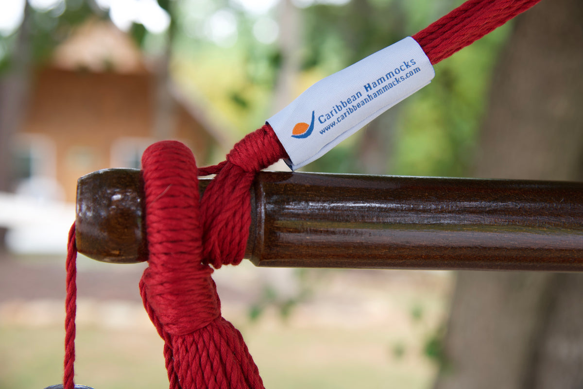The dark varnished hardwood spreader bar of a red Island Haven hammock chair, with end cords looped over it and a wooden bead hanging below