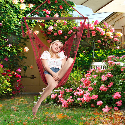 Woman reclining in a red Island Haven hammock chair in a garden surrounded by climbing roses
