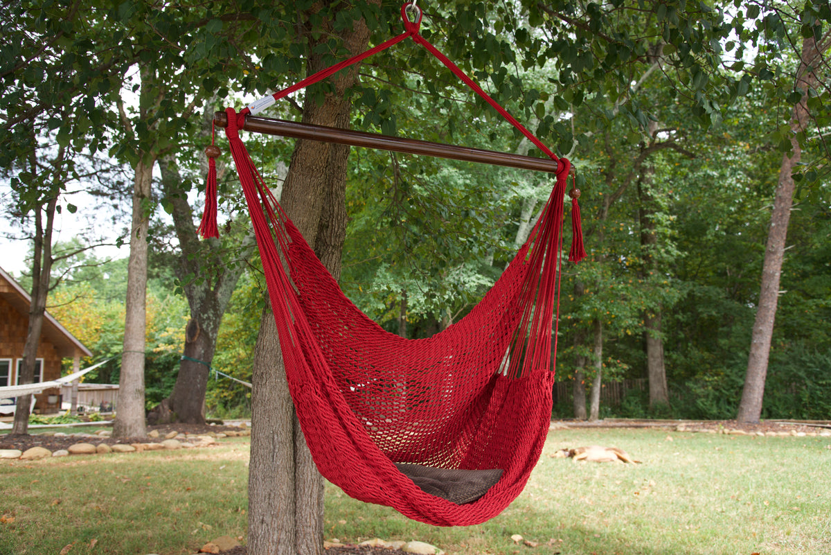Red Island Haven hammock chair with a brown seat pillow, hanging from a tree in a wooded backyard with a timber cabin behind