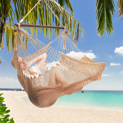 Woman resting in a tan Island Haven hammock chair hung from a palm tree above a white sand beach