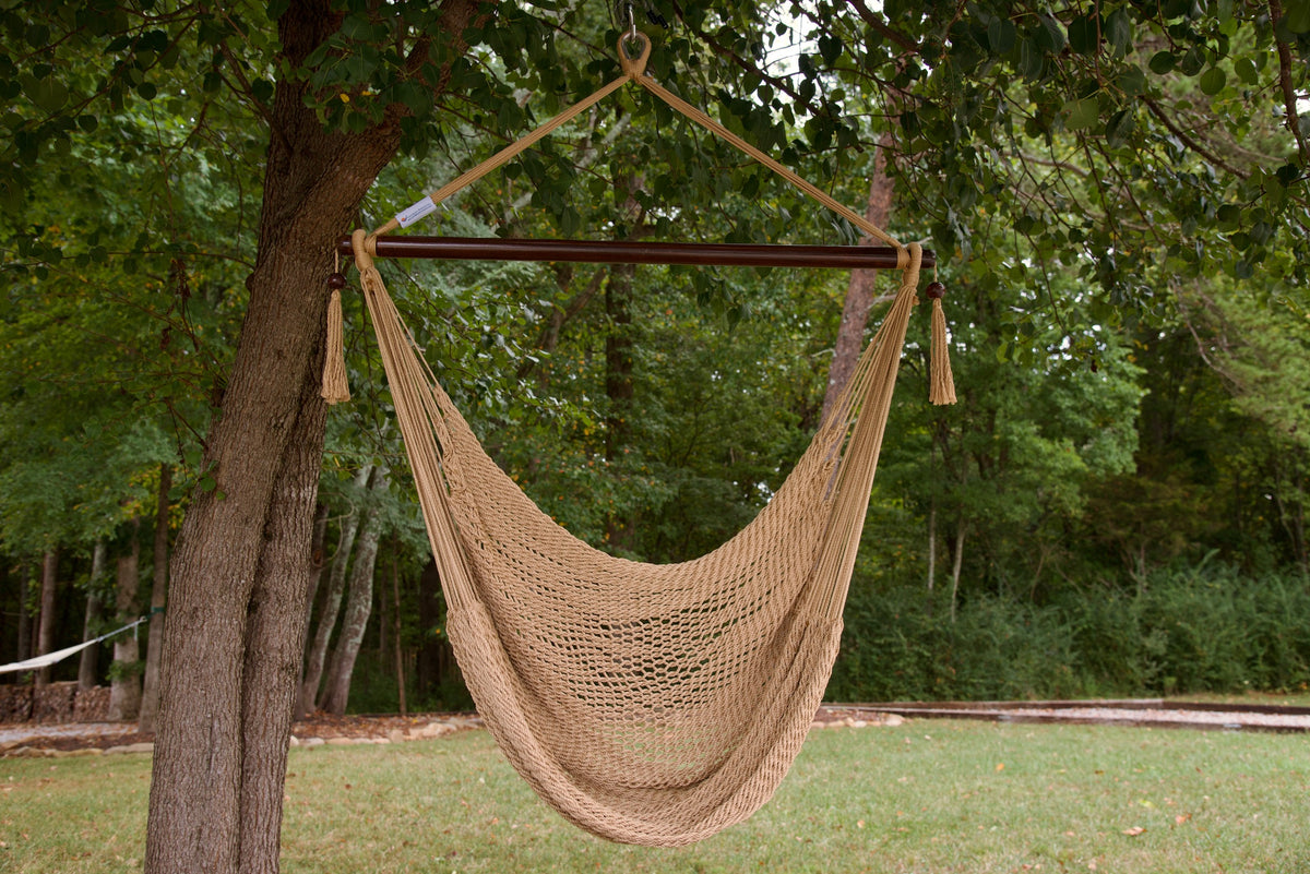 Tan Island Haven hammock chair hanging from a shade tree in a mown backyard with woods behind