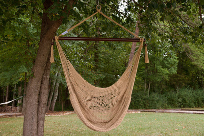 Tan Island Haven hammock chair hanging from a shade tree in a mown backyard with woods behind