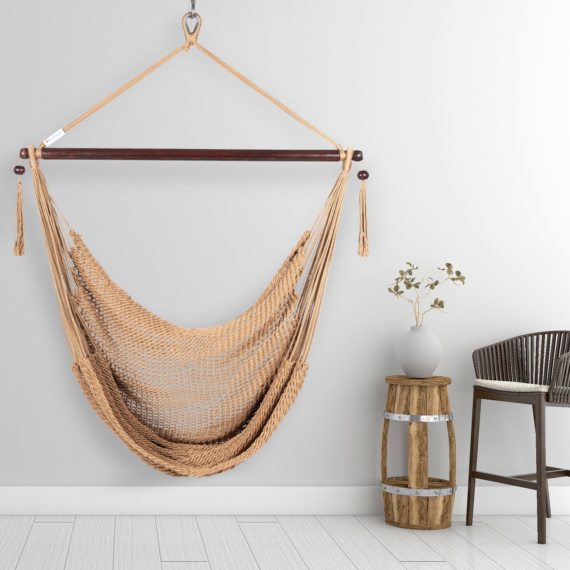 Tan Island Haven hammock chair hanging beside a barrel side table and bar stool against a pale grey wall