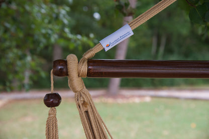 The dark varnished hardwood spreader bar of a tan Island Haven hammock chair, with end cords looped over it and a wooden bead hanging below