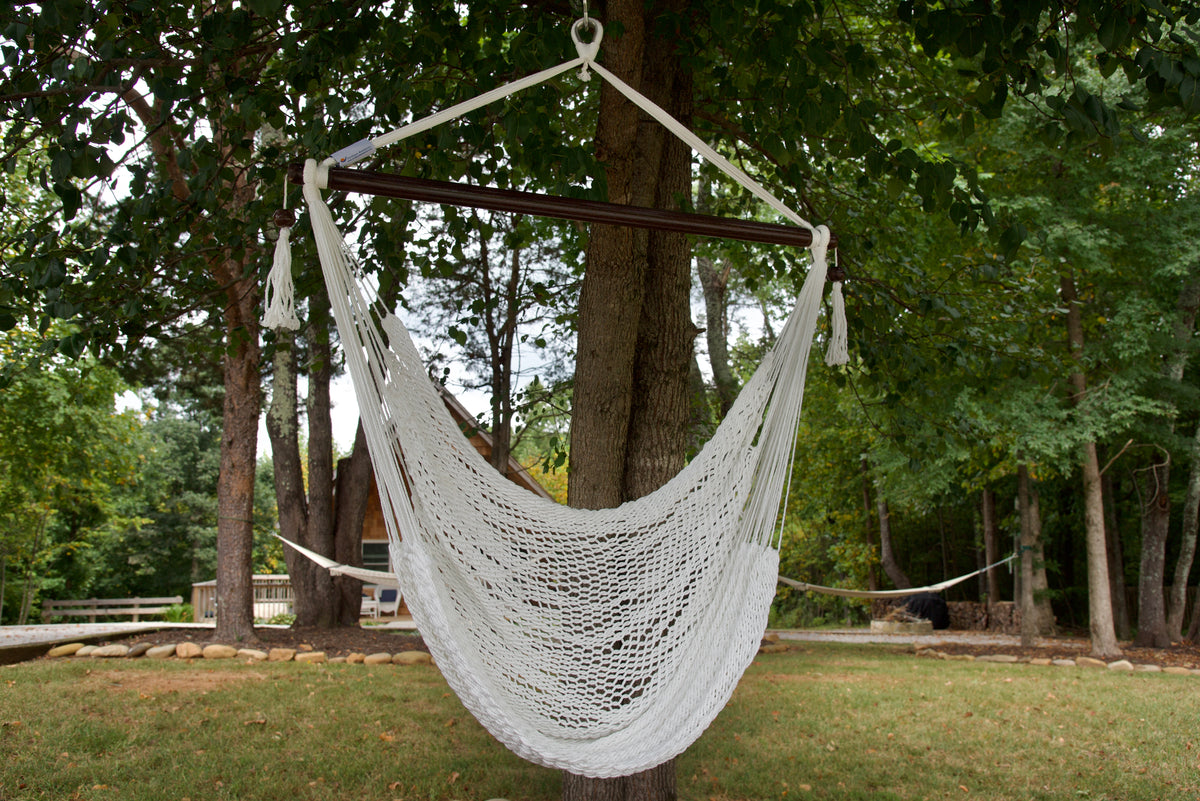 White Island Haven hammock chair hanging from a shade tree in a mown backyard with woods behind