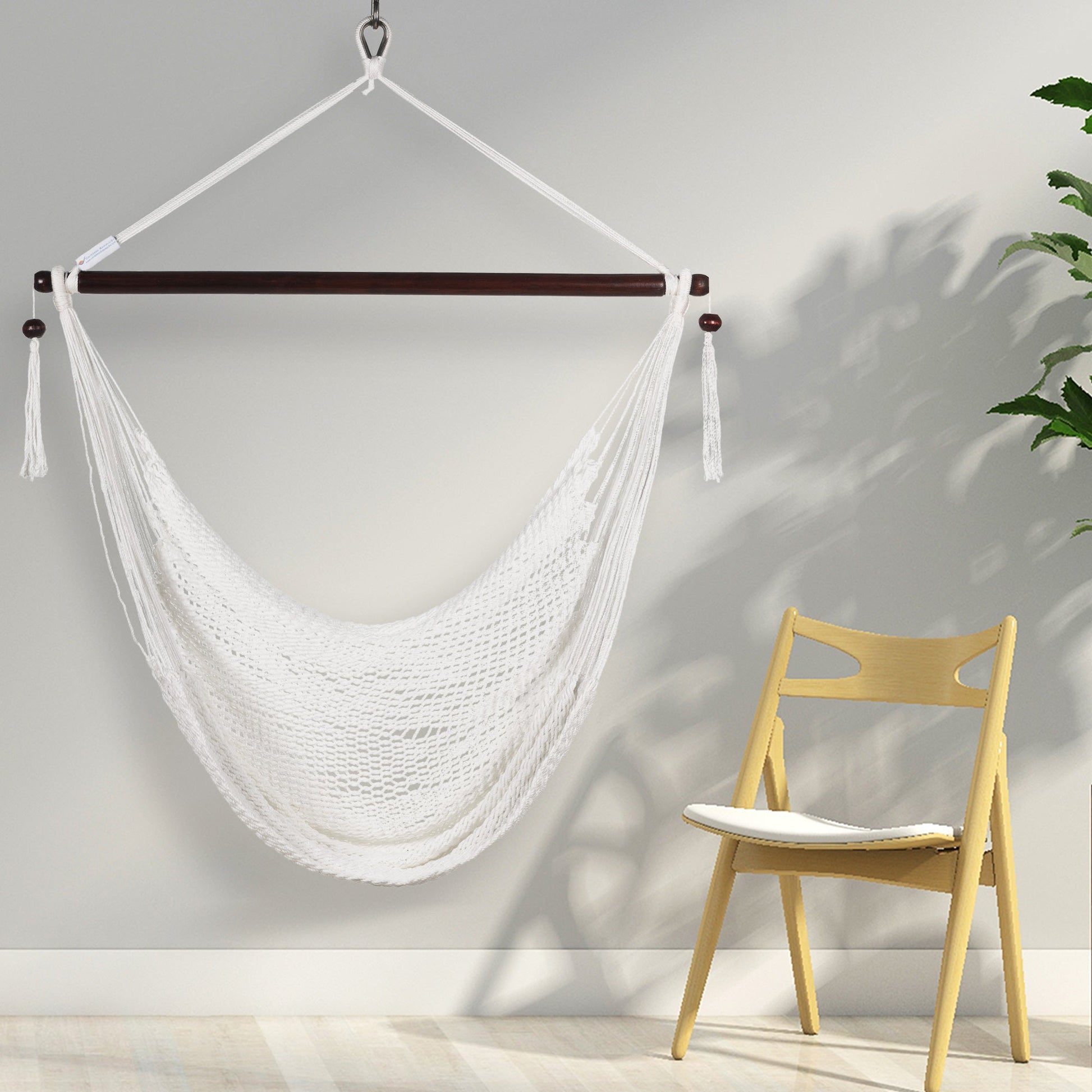 White Island Haven hammock chair hanging beside a light wooden chair against a pale wall