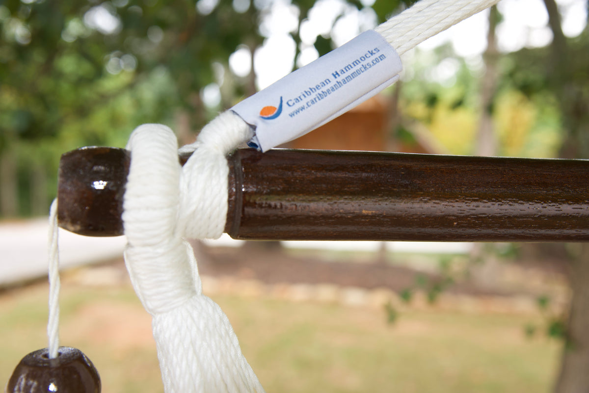 The dark varnished hardwood spreader bar of a white Island Haven hammock chair, with end cords looped over it and a wooden bead hanging below