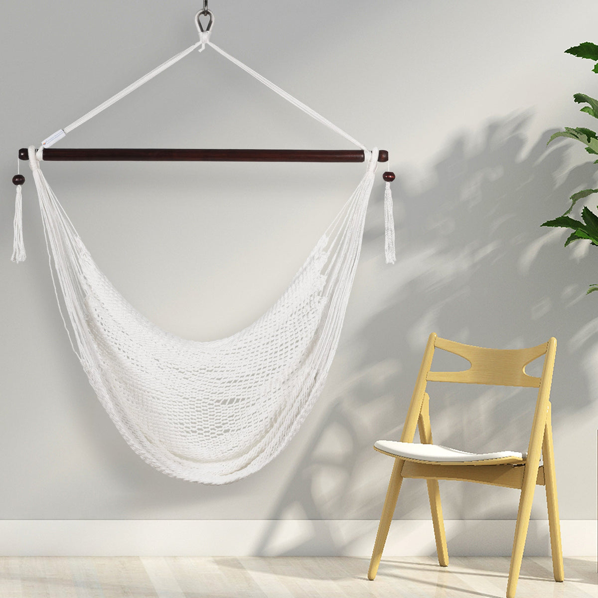 White Island Haven hammock chair hanging beside a light wooden chair against a pale wall