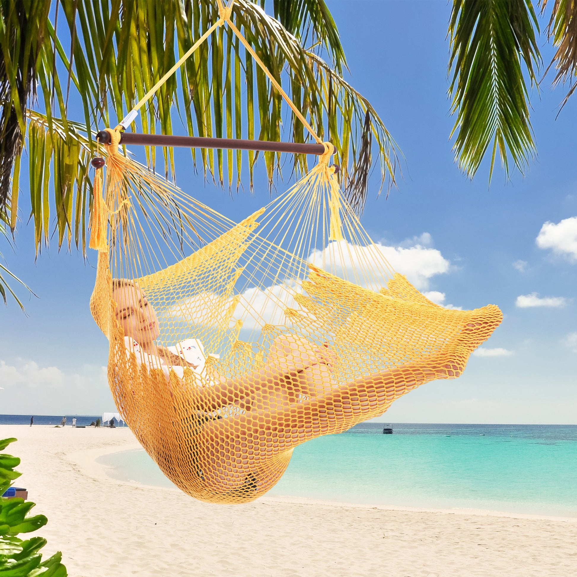 Woman resting in a yellow Island Haven hammock chair hung from a palm tree above a white sand beach