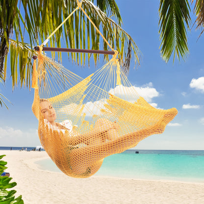 Woman resting in a yellow Island Haven hammock chair hung from a palm tree above a white sand beach