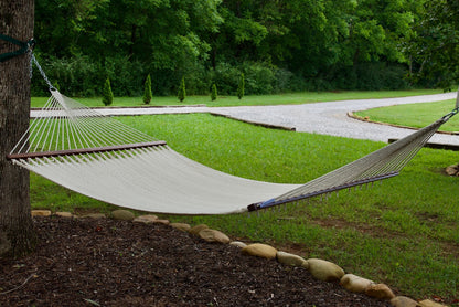 Cream Island Oasis hammock hung from a tree in a green backyard with a gravel path behind