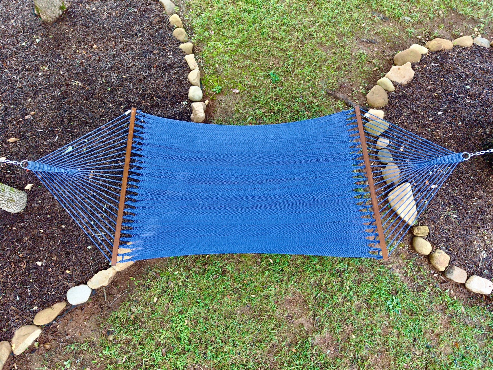 Overhead view of a dark blue Island Oasis hammock hung between two stone-edged garden beds