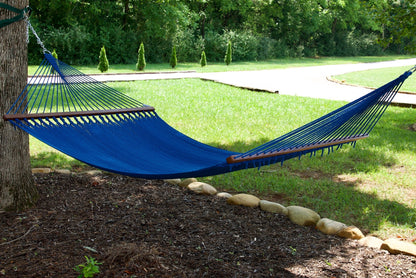 Dark blue Island Oasis hammock hung between a tree and a post in a green backyard with a gravel path behind