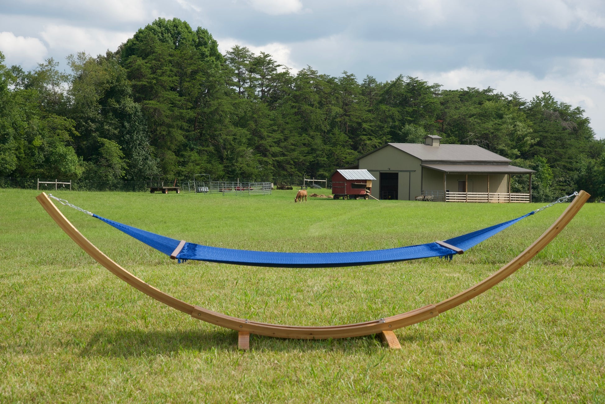 Dark blue Island Oasis hammock hanging on the Wood Arc Hammock Stand in a pasture with a barn behind