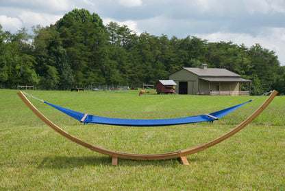 Dark blue Island Oasis hammock hanging on the Wood Arc Hammock Stand in a pasture with a barn behind